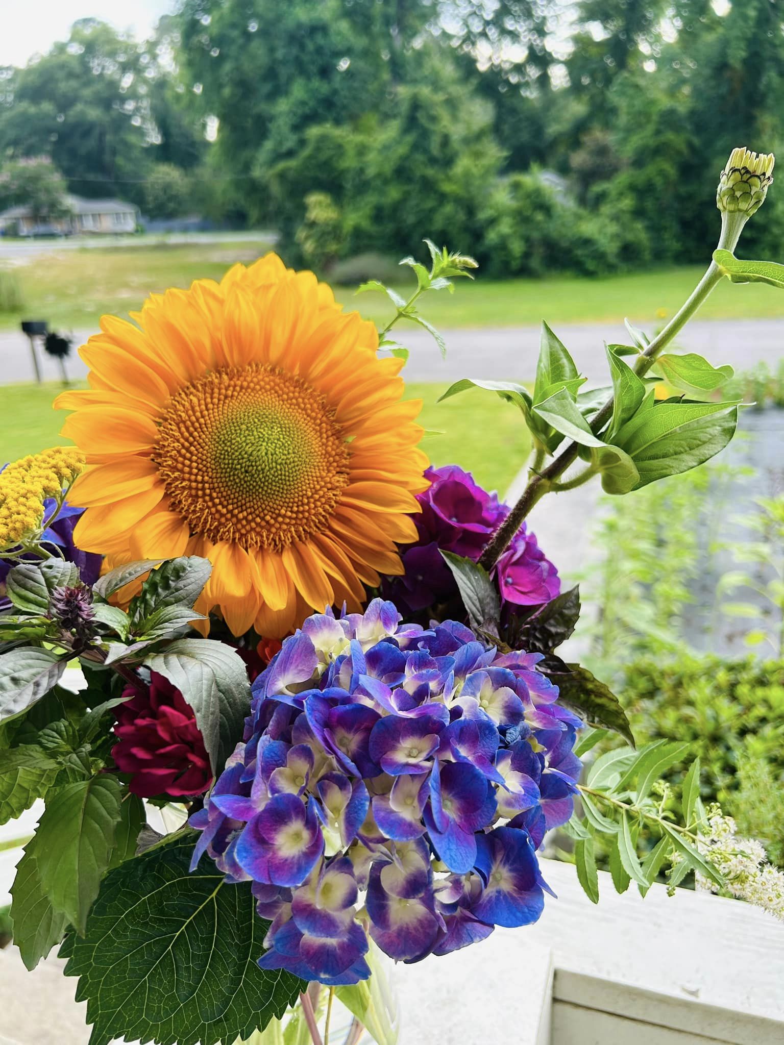 a bouquet of colorful flowers including a purple hydrangea and a large yellow sunflower